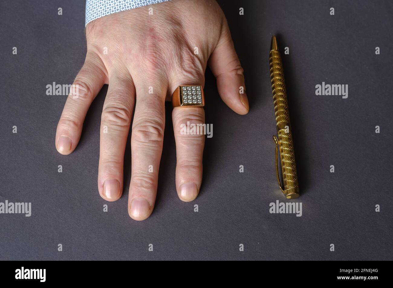Eine Hand mit goldenem Ring und Stift auf grauem Hintergrund. Die rechte  Hand eines erwachsenen Mannes mit einem Siegelring auf seinem Zeigefinger.  Draufsicht Stockfotografie - Alamy