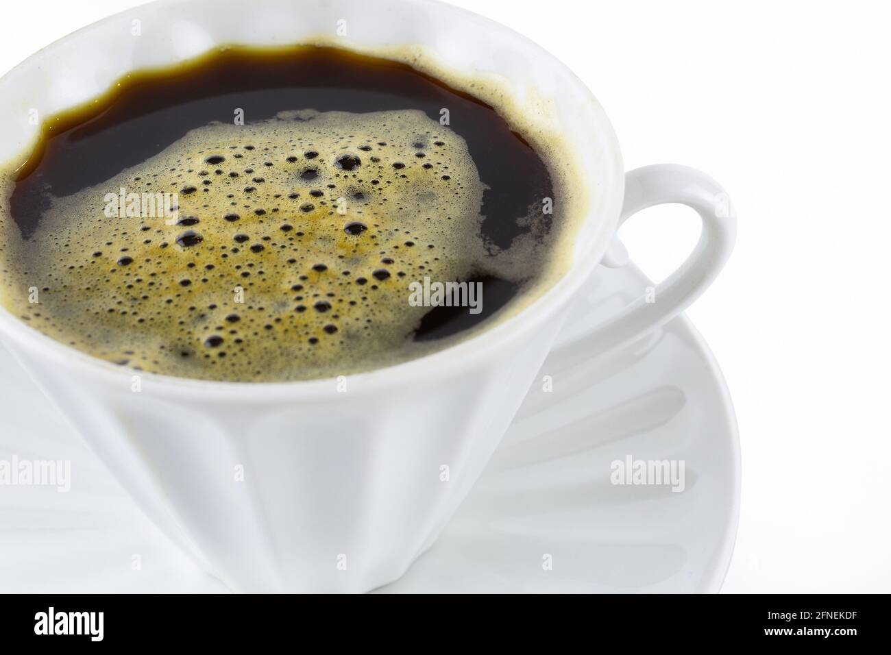 Weiße Porzellantasse mit Kaffee mit Schaum und Untertasse auf weißem Hintergrund, Nahaufnahme Stockfoto