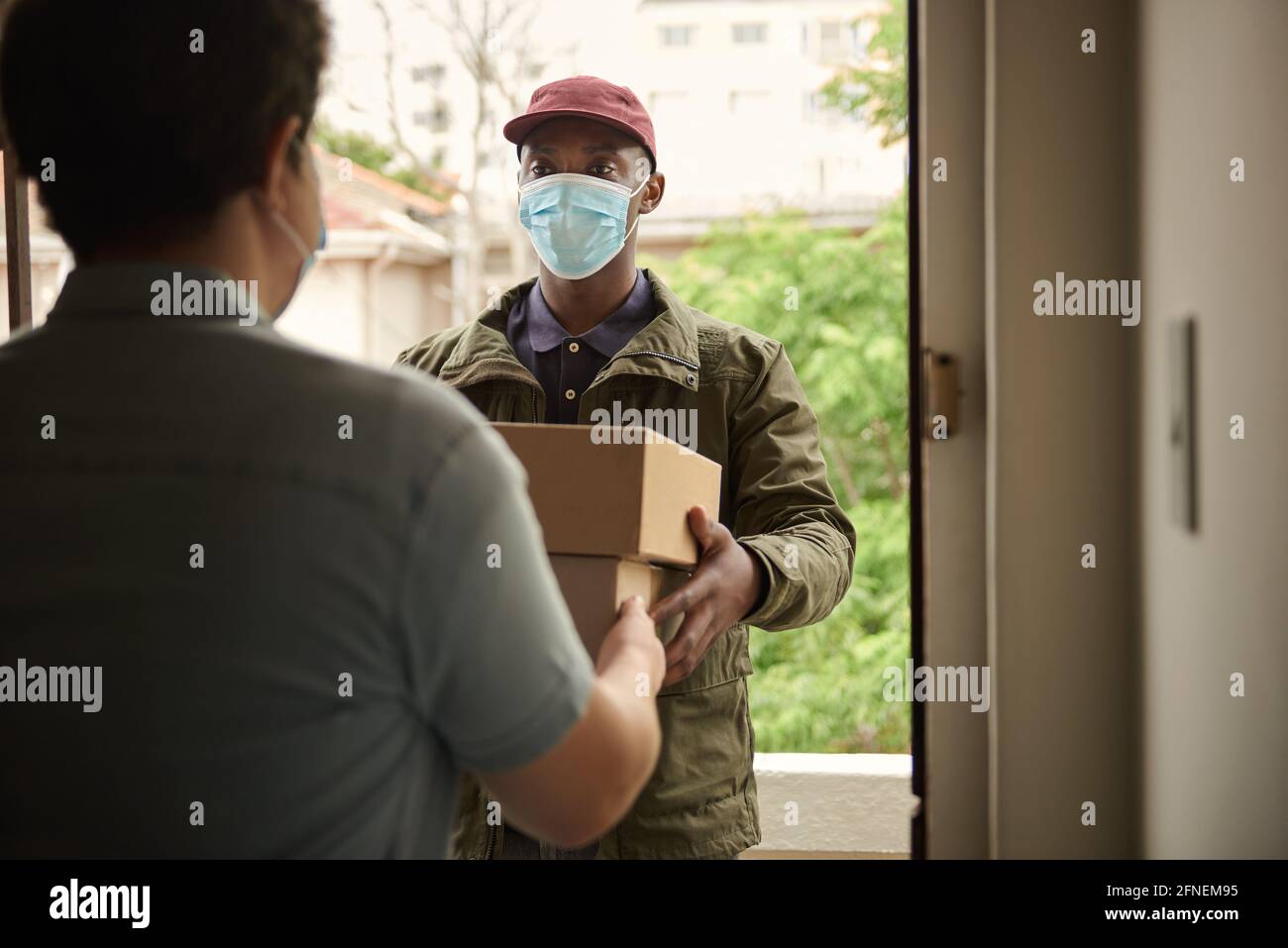 Afrikanischer Kurier in einer Maske, der Pakete an einen Kunden liefert Stockfoto