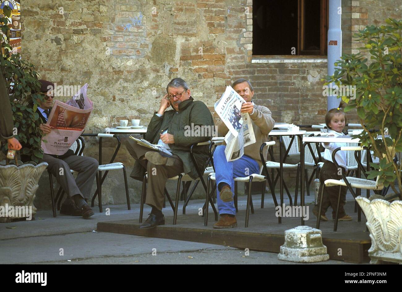Männer lesen die Tageszeitung in einem italienischen Straßencafé in Bounconvento. [Automatisierte Übersetzung] Stockfoto