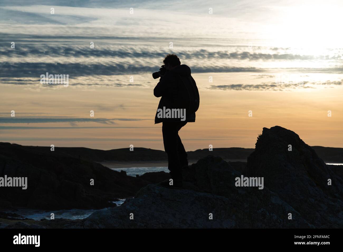 Silhouette eines Fotografen mit einer Kamera in den Händen auf einem Hintergrund des Himmels bei Sonnenaufgang auf der Insel Houat, Frankreich Stockfoto