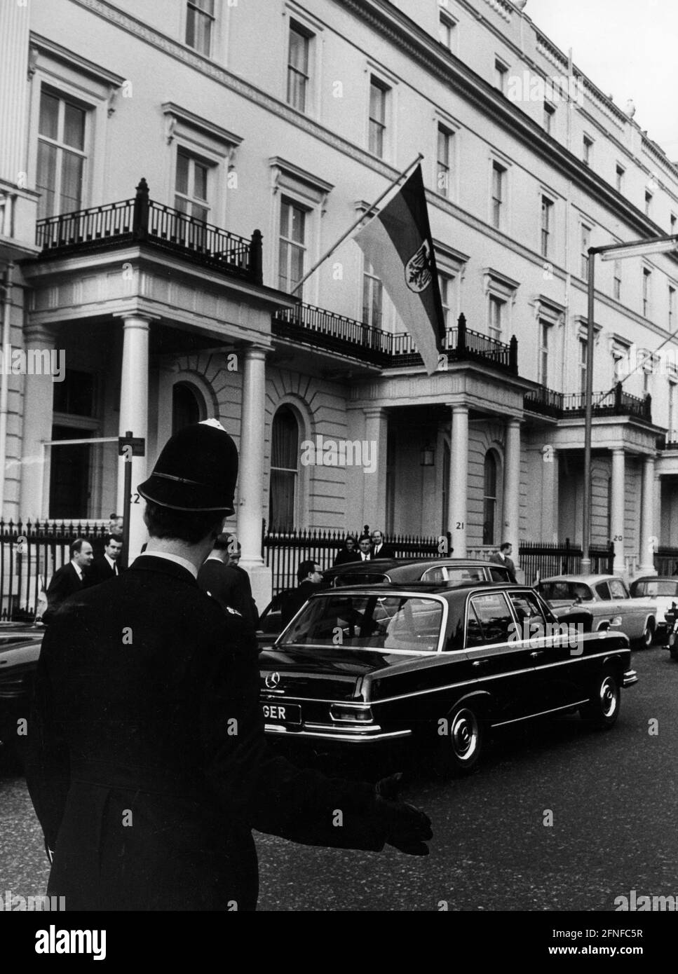 Vor der deutschen diplomatischen Vertretung stehen ein paar Autos und ein Polizist in Uniform. An der Wand hängt die Flagge der Bundesrepublik Deutschland. Undatierte Fotografie. [Automatisierte Übersetzung] Stockfoto