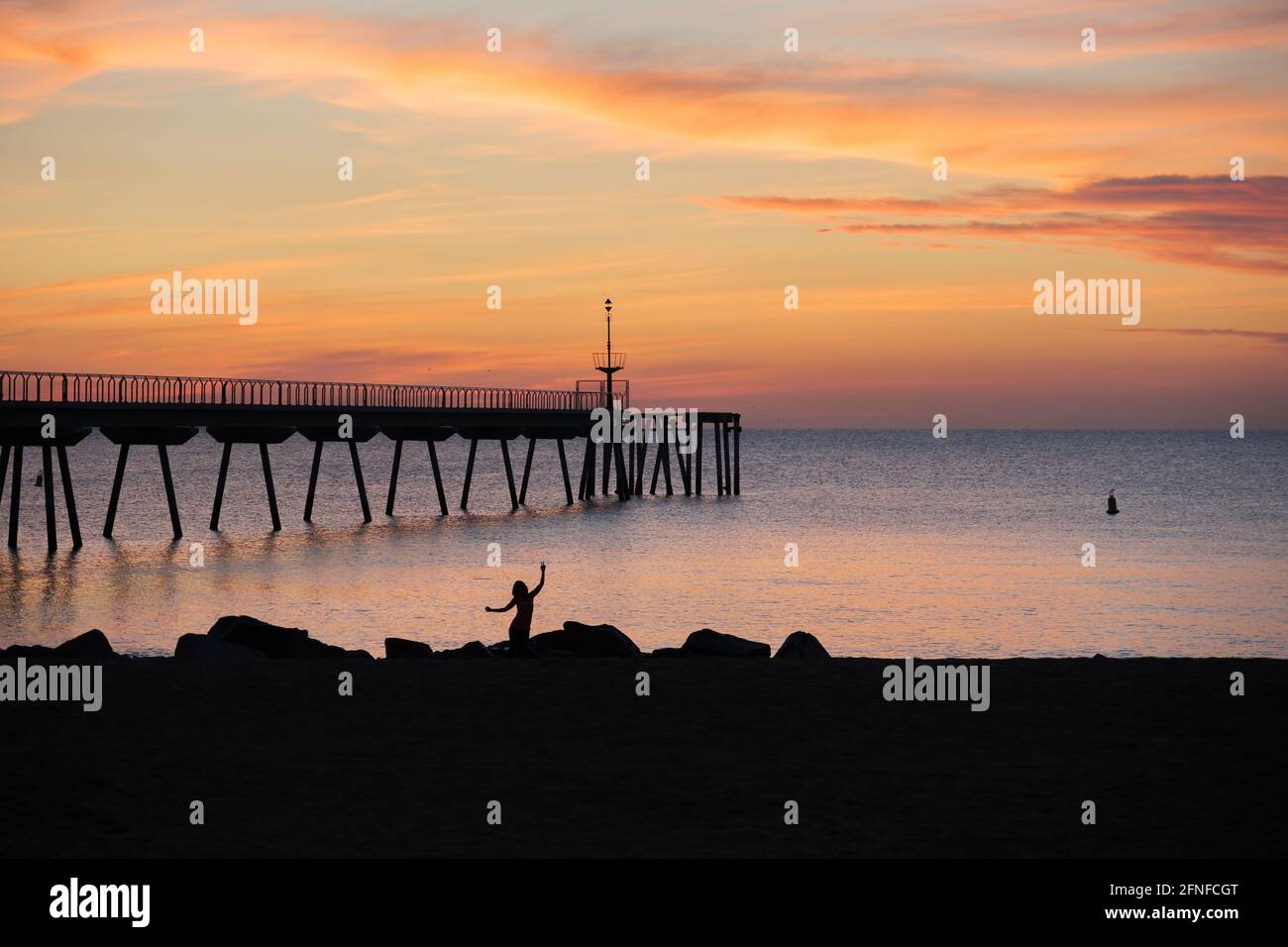 Silhouette einer Frau, die morgens am Strand tanzt. Sonnenaufgang im mittelmeer mit Blick auf den Ponton. Stockfoto