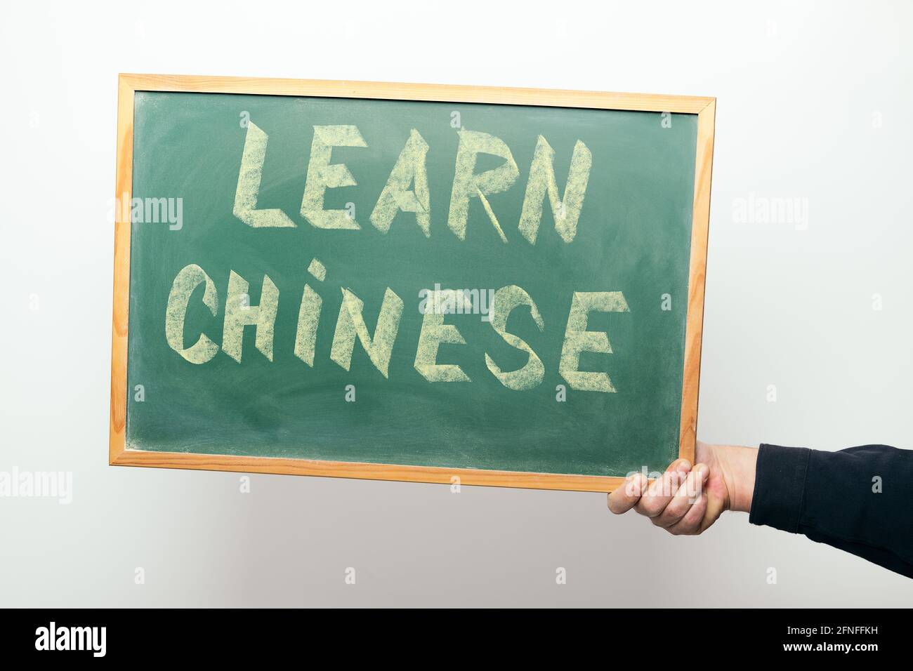 Die Hand, die eine Tafel mit der Botschaft HÄLT, LERNT CHINESISCH handschriftlich In Kreide Stockfoto