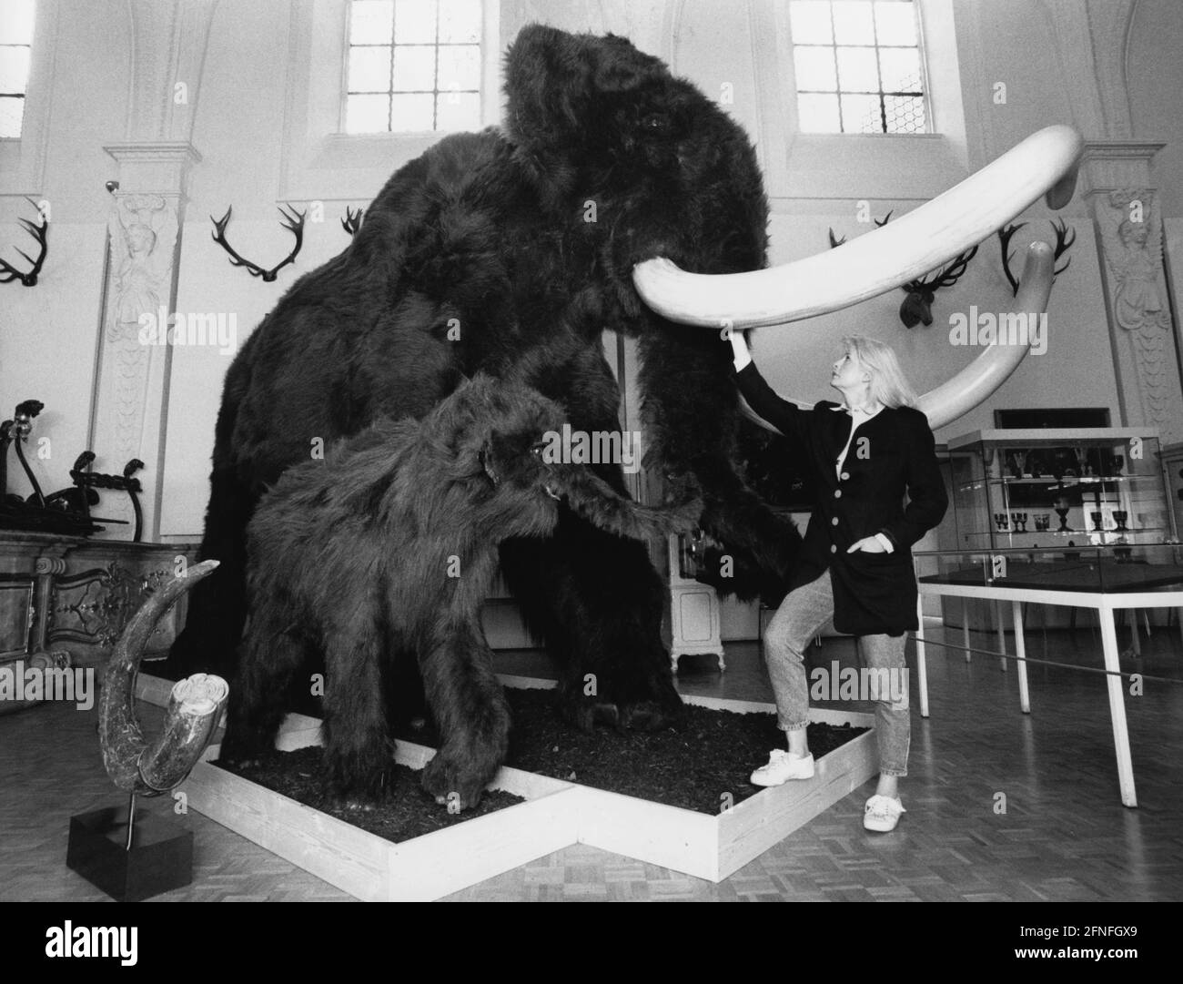 Nachbildung eines wolligen Mammuts mit jungen Menschen in einer Ausstellung über die Jagd in der Steinzeit im Weißen Saal des Museums. [Automatisierte Übersetzung] Stockfoto