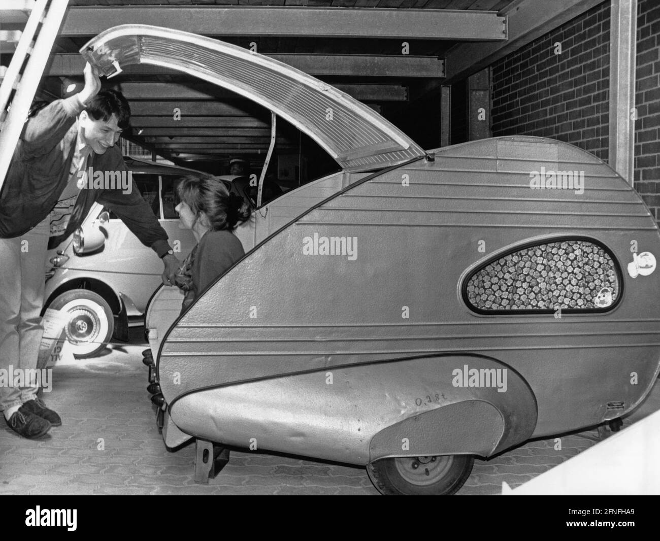 „eine Frau sitzt in der offenen Heckklappe eines Piccolino, der im Störy Automobilmuseum ausgestellt ist. Der Piccolino wurde als ''wahrscheinlich der kleinste nutzbare Wohnwagen der Welt'' vermarktet. Er wog nur 130 kg und kostete 856.75 1955 DM neu. [Automatisierte Übersetzung]' Stockfoto