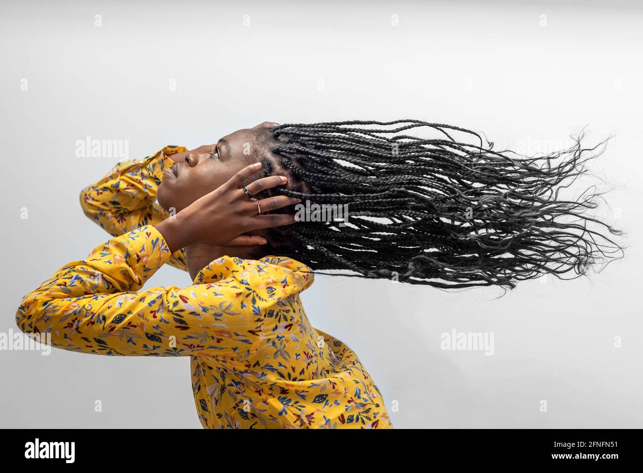 Seitenansicht einer sorglosen afroamerikanischen Hündin mit langem Fliegen Geflochtene Haare auf grauem Hintergrund Stockfoto