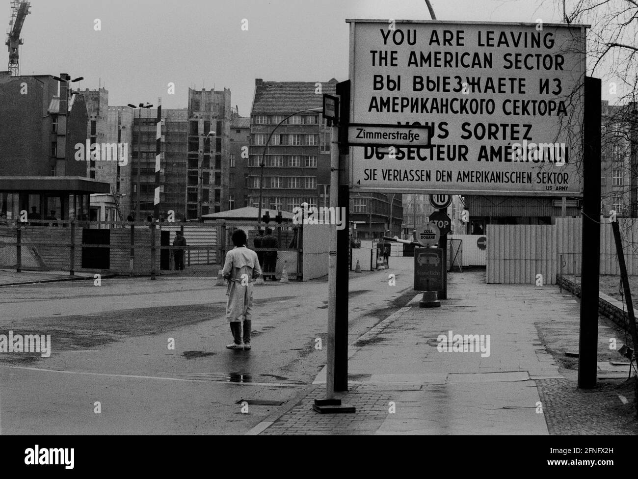 Berlin-Bezirke / DDR-Mauer / 1985 Checkpoint Charly. Der Grenzübergang zwischen Kreuzberg und Mitte ist für Ausländer, darunter Diplomaten, reserviert. Sie werden vom deutschen Zoll, einem Hilfsorgan der Westalliierten, abgeräumt. Zwei Geschäftsleute gehen nach Ost-Berlin. Am Checkpoint Charly standen sich amerikanische und sowjetische Panzer während des Mauerbaus 1961 gegenüber. Viersprachiges Zeichen der 4 Alliierten: Sie verlassen den amerikanischen Sektor // Berliner Status / Checkpoint / Grenze / Bezirke / // Geschichte / Alliierten / Kommunismus / Sowjets [automatisierte Übersetzung] Stockfoto