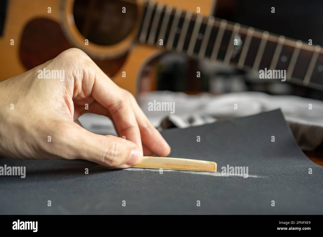 Senken Sie die Höhe einer akustischen Gitarre Sattel für eine Bessere Spielbarkeit durch Abschleifen eines Knochensattels mit Schleifpapier Stockfoto