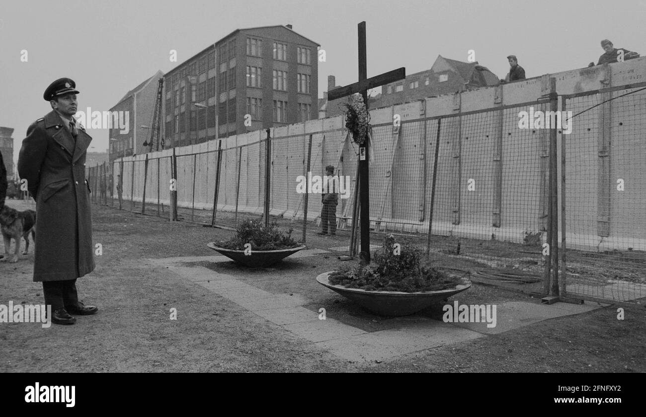 Berlin-Bezirke / Kreuzberg / Wall / 1980 Alltag an der Mauer mit einem britischen Offizier. Er steht vor der Mauer in der Zimmerstraße am Holzkreuz für das Maueropfer Peter Fechter. DDR-Grenzposten sind dabei, die Mauer zu modernisieren. Die Grenzsoldaten vor der Mauer achten darauf, dass die Grenzsoldaten, die die Mauer bauen, nicht weglaufen. Hinten Checkpoint Charly, links Kreuzberg, rechts Berlin-Mitte // British / Dead / Mitte / Allied / [automatisierte Übersetzung] Stockfoto