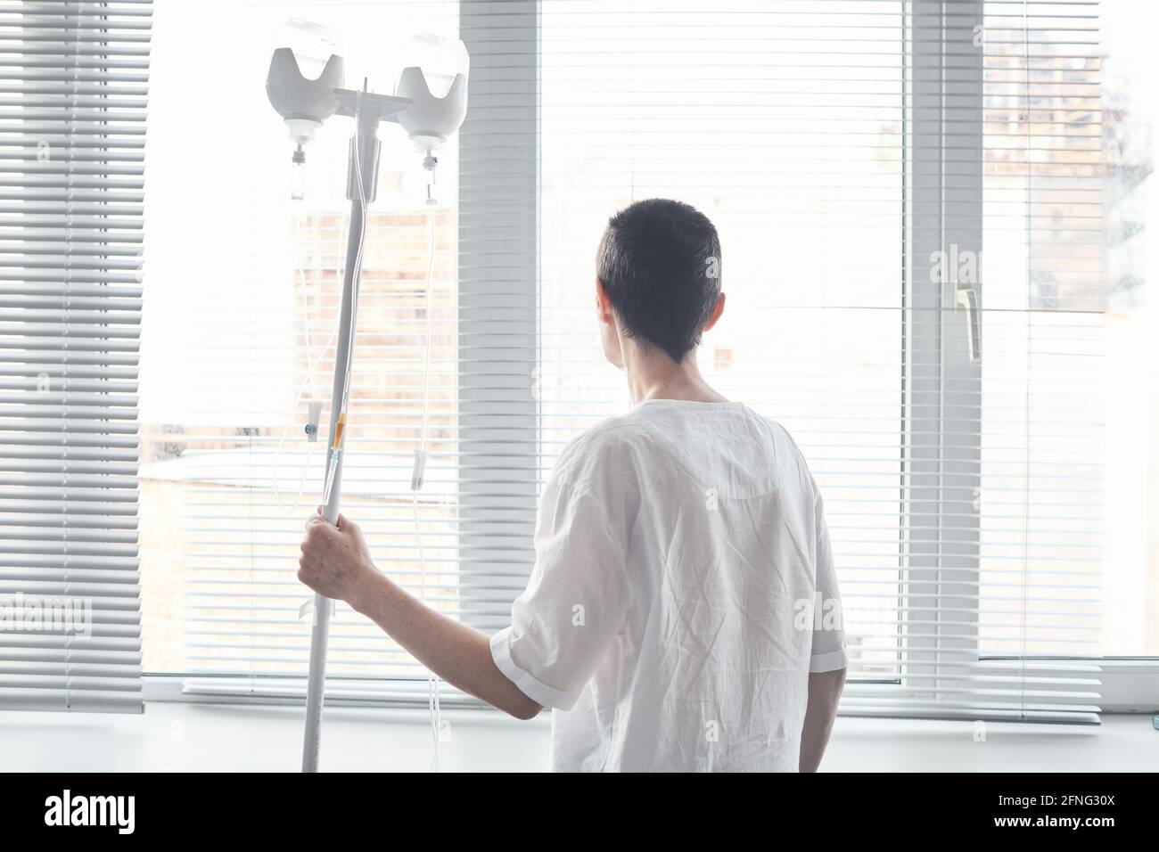 Rückansicht des Patienten mit Pipette, die vor dem steht Das Fenster auf der Krankenstation Stockfoto