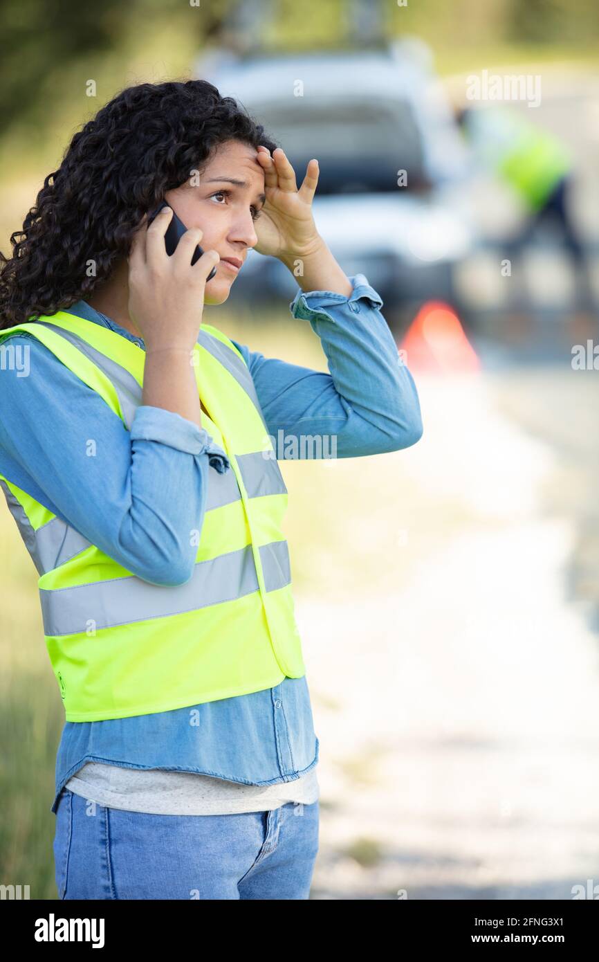 Frau in Sicherheitsweste Telefone mit Autoservice nach der Panne Stockfoto