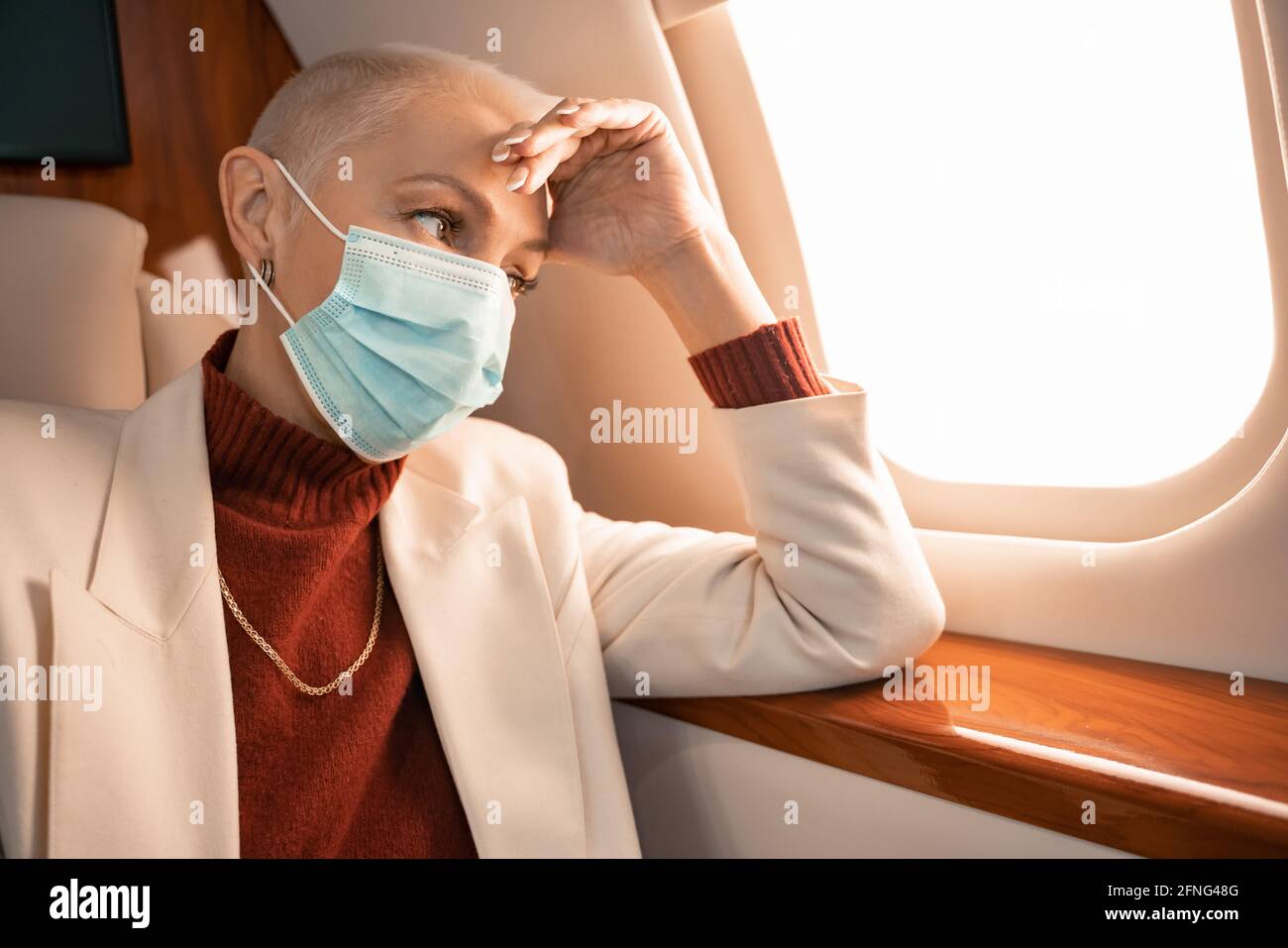 Reife Geschäftsfrau in medizinische Maske Blick auf Fenster in privat Ebene Stockfoto