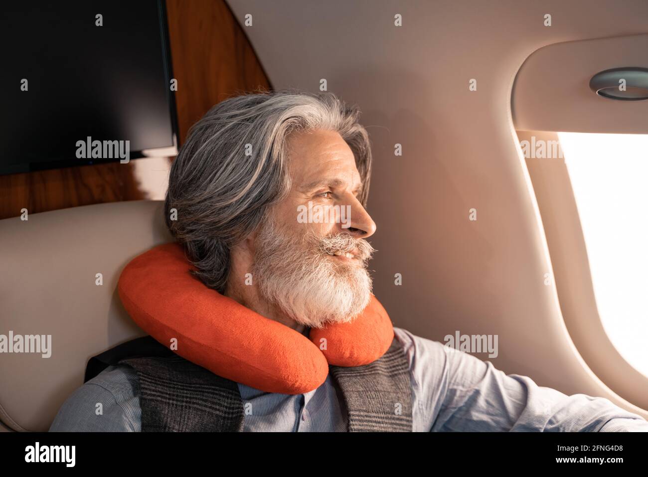 Lächelnder Mann im Nackenkissen, der privat auf das Fenster schaute Ebene Stockfoto