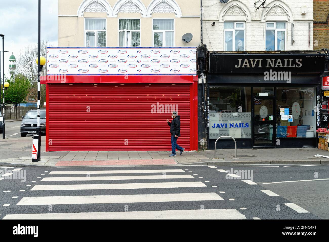 Ein asiatischer Mann, der eine Maske trägt und an einem geschlossenen vorbeiläuft Kaufen Sie mit roten Schalungen neben einem Javi Nails Geschäft In Kings Road Southall London, England, Großbritannien Stockfoto
