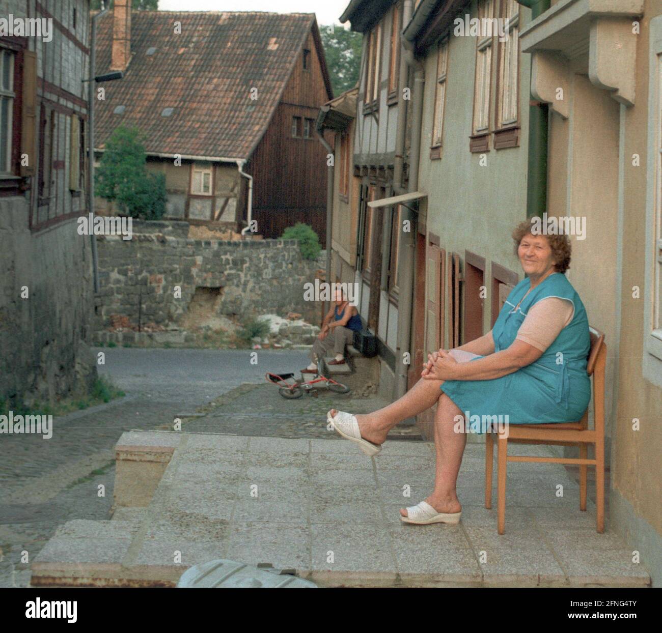 Sachsen-Anhalt / DDR Land / 1990 Quedlinburg, mittelalterliche Reichsstadt: Altstadt an der Stiftskirche, Frauen sitzen abends vor den Wohnungen // Menschen / Quedlinburg wurde 919 nach der Wahl des ersten deutschen Königs, des sächsischen Herzogs Heinrich, zum Kaiserpalast. Sein Sohn, Otto I., ließ 936 an der Stelle des Palastes ein Frauenkloster errichten. In der Stiftskirche, die seit 1100 erbaut wurde, wird der berühmte Domschatz aufbewahrt. Es wurde nach dem letzten Krieg von den Amerikanern gestohlen und 1993 von der Familie des Diebes für 3 Millionen Euro zurückgekauft. Die Kathedrale ist Teil der Stockfoto