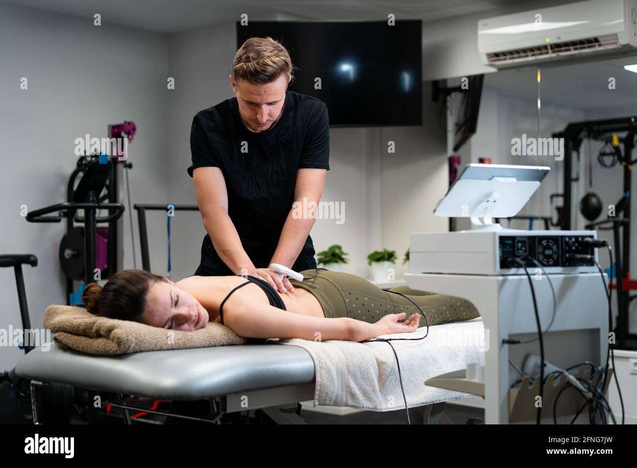 Männlicher Physiotherapeut, der während der Behandlung Laser auf die Rückenhaut des Weiblichen anwendet Medizinische Behandlung im Krankenhaus Stockfoto