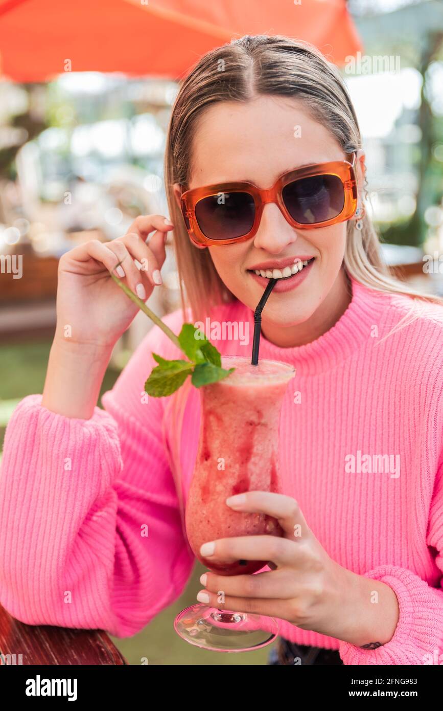 Crop verträumt weiblich in rosa Pullover sitzen am Tisch mit Köstlicher, kalter Beerencocktail in der Bar im Freien und beim Betracht Kamera Stockfoto