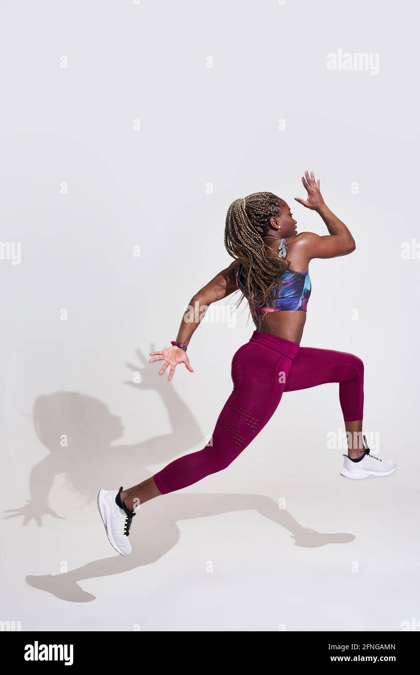 Seitenansicht der entschlossenen afroamerikanischen Sportlerin, die beim Ausdauertraining mit fliegenden Haaren springt und nach vorne blickt Stockfoto