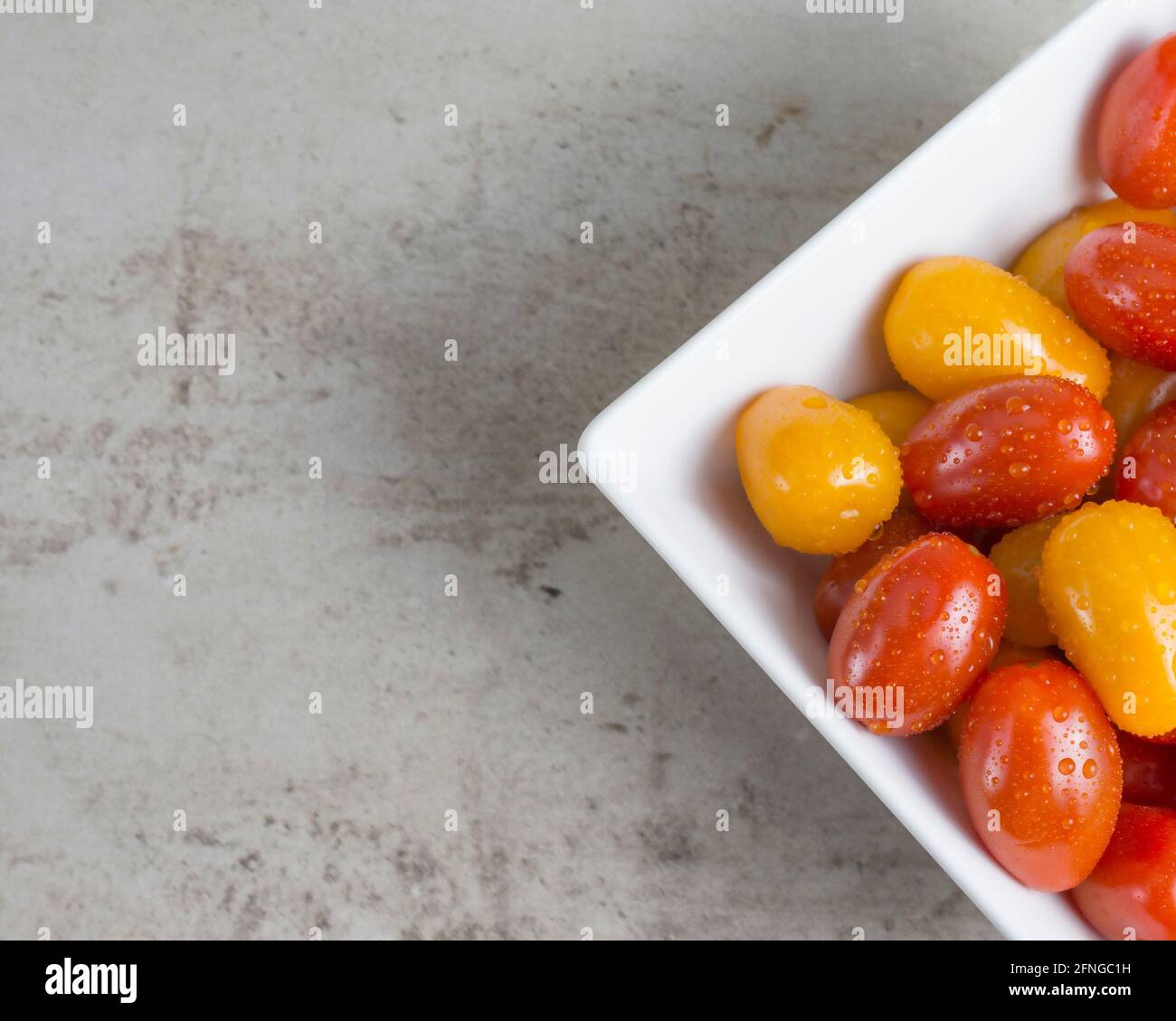 Rote und gelbe kleine Tomaten in einer weißen quadratischen Schüssel. Flach liegend Stockfoto