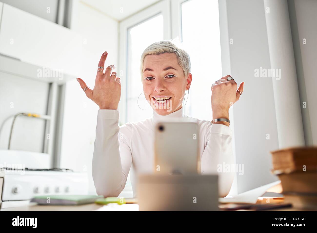Lächelnde Bloggerin, die während der Videoaufnahme über Astrologie spricht Handy am Schreibtisch bei Sonnenlicht Stockfoto