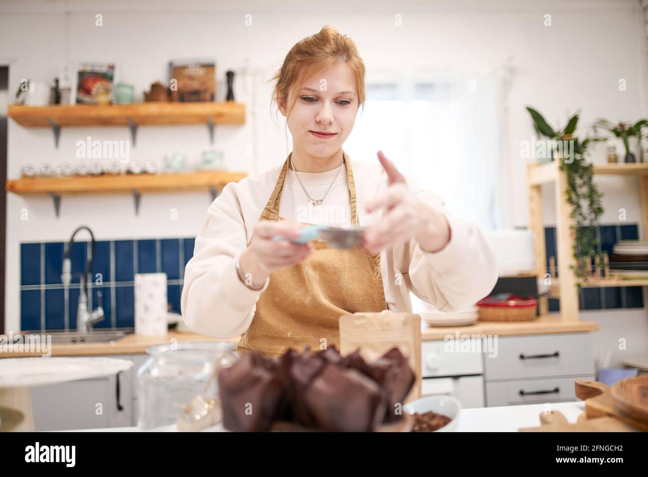 Lächelndes junges Weibchen mit Sieb, das Muffins in Backbechern streut Mit Puderzucker in der Hausküche Stockfoto