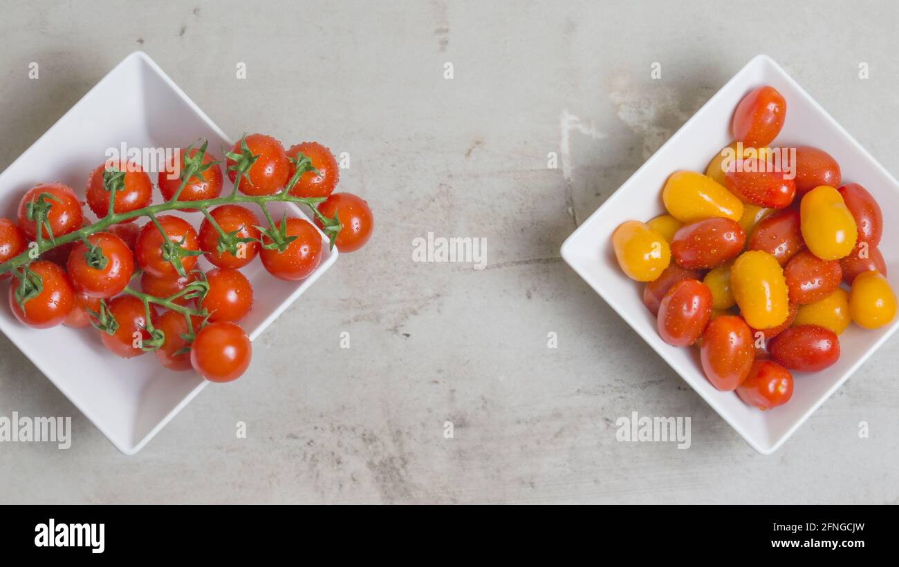 Zweig aus roten kleinen Tomaten und farbigen Tomaten in einer weißen quadratischen Schüssel. Flach liegend. Stockfoto