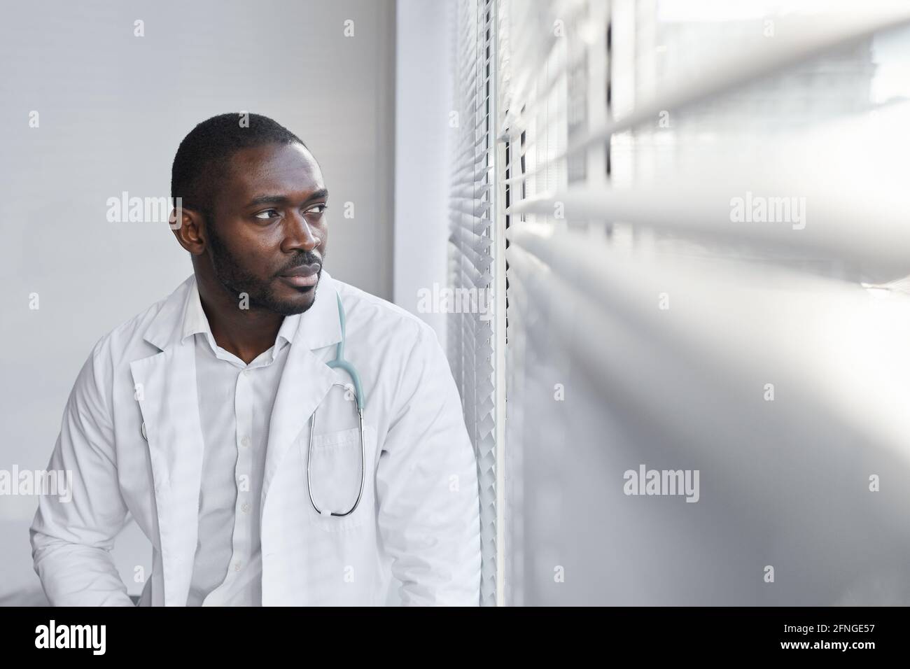 Afrikanischer junger Arzt, der in der Nähe des Fensters im Krankenhaus und sitzt Blick auf die Ansicht Stockfoto