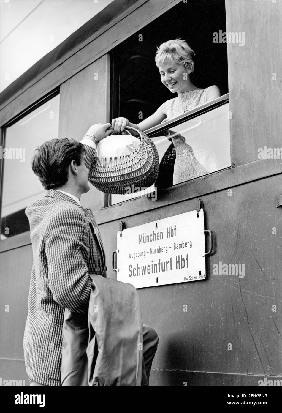 Frau erhält einen gefüllten Korb, der ihr von einem übergeben wird Mann durch das Zugfenster [automatisierte Übersetzung] Stockfoto