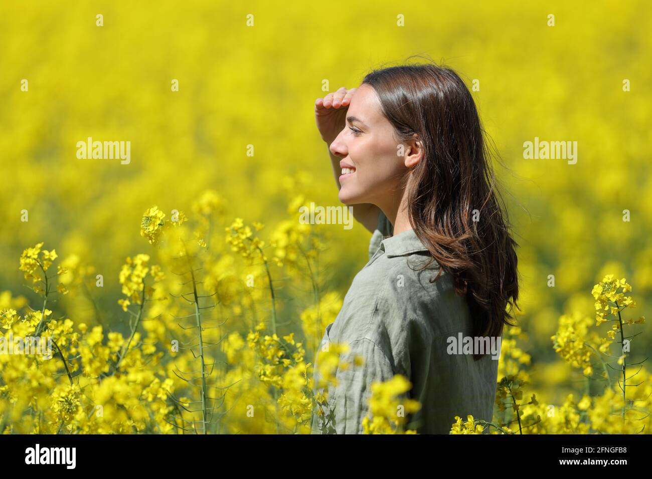 Glückliche Frau, die vor der Sonne schützt, mit ihrer Hand in einem Gelb blühtes Feld Stockfoto