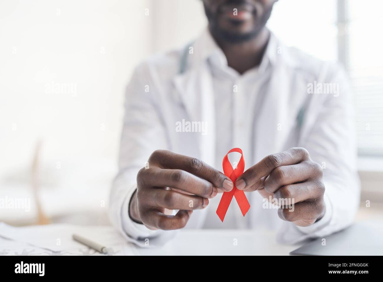 Nahaufnahme eines afrikanischen Arztes mit rotem Band in den Händen Im Krankenhaus Stockfoto