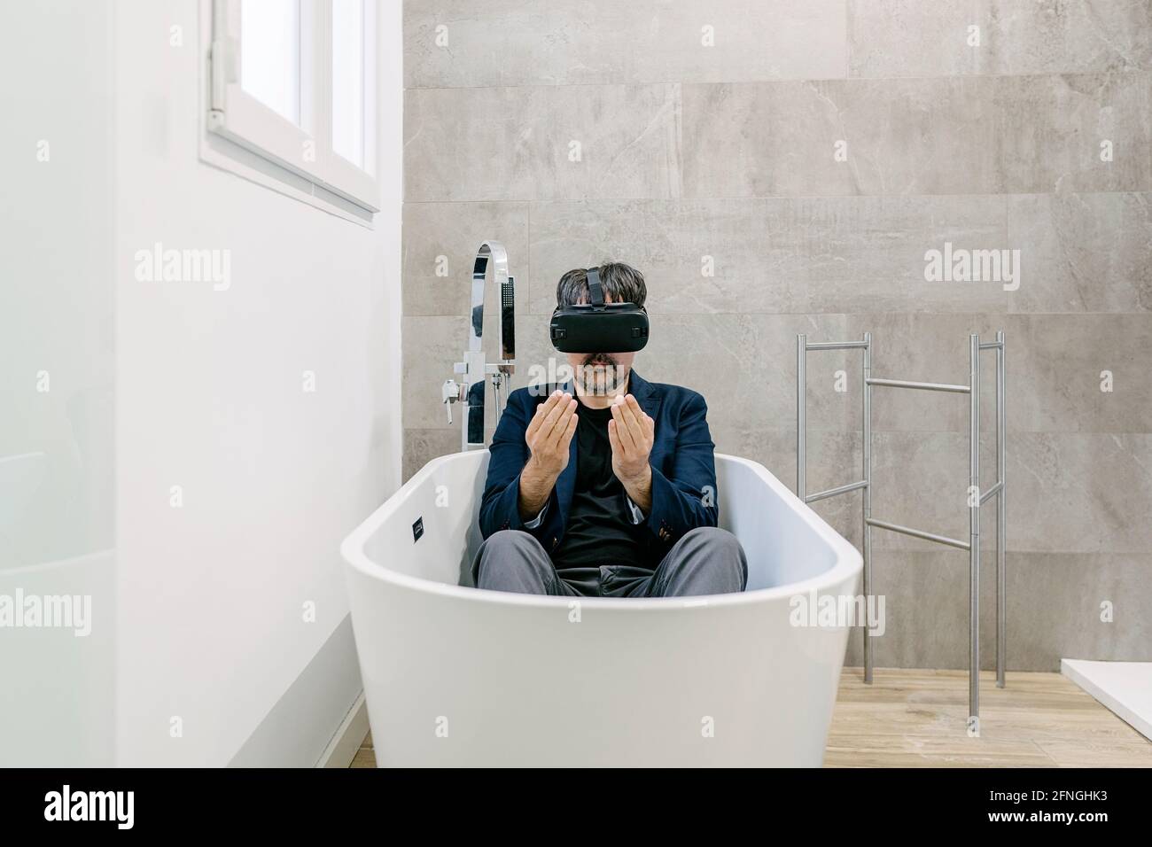 Vollständig bekleideter, eleganter erwachsener Mann, der in einer Badewanne virtuelle Realität erlebt, als wäre er an einem tropischen Strand. Virtual-Reality-Brille. Virtuelle Realität Stockfoto