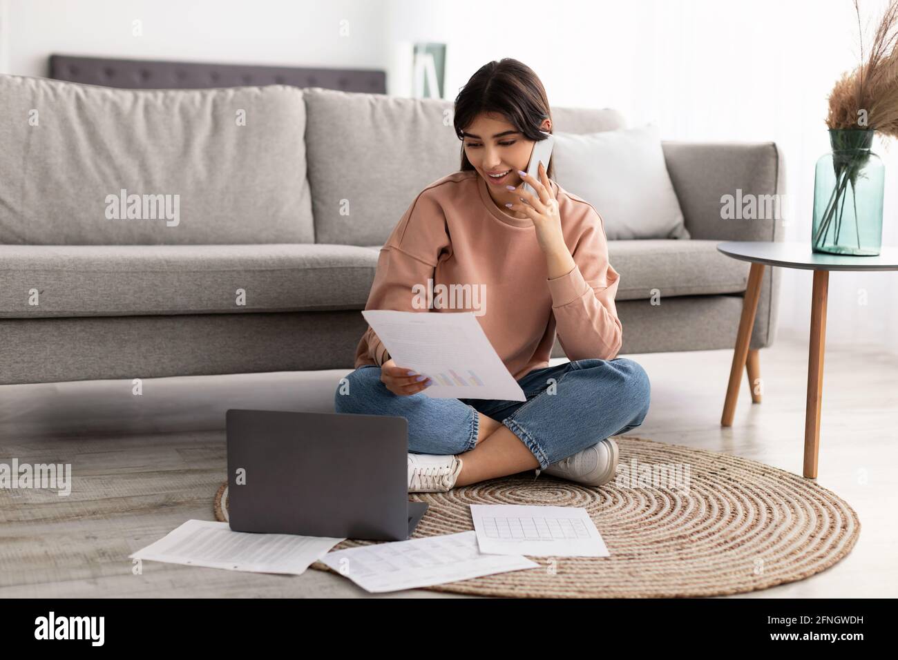 Frau, die einen Bericht über das Lesen in Papierform hält und zu Hause telefoniert Stockfoto