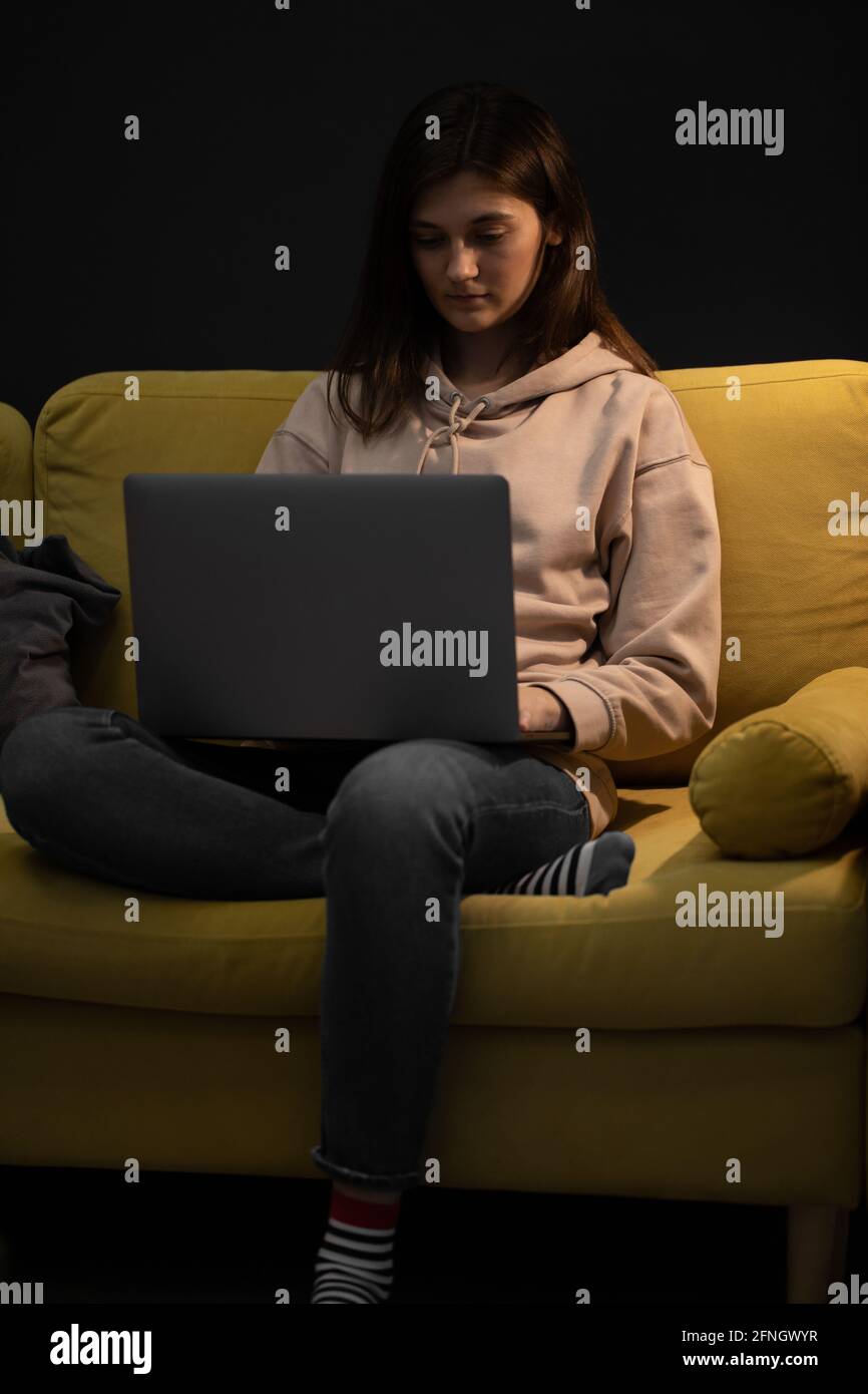 Brunette Mädchen sitzt auf der Couch mit Laptop unter Spotlampe Online kommunizieren Stockfoto