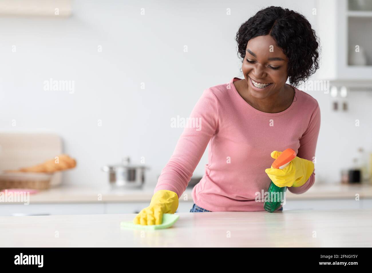 Fröhliche afroamerikanische junge Frau in Gummihandschuhen Reinigungstisch Stockfoto