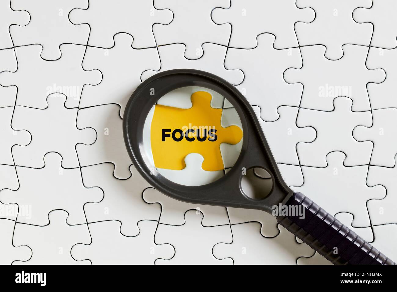 Das Wort Fokus auf fehlende Puzzle-Stück mit einer Lupe. Um ein Motiv zu fokussieren oder sich auf es zu konzentrieren. Stockfoto