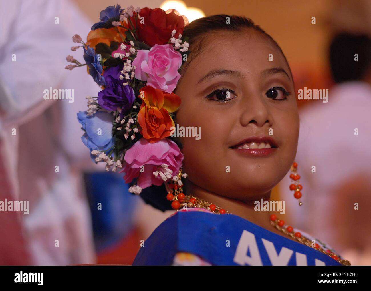 Porträt einer jungen und unbekannten lateinischen Tänzerin, die lächelt und das Kleid der Stadt Merida in Mexiko trägt, auf ihrem Kopf hat sie eine Krone aus bunten Blumen d Stockfoto