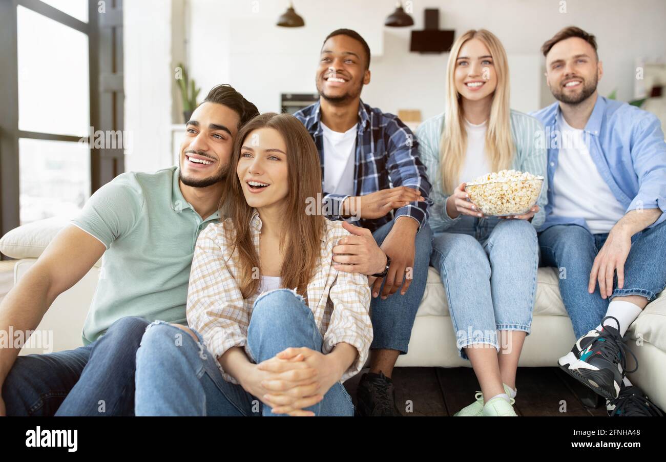 Eine Gruppe fröhlicher junger Freunde, die zu Hause einen Film genießen, Popcorn essen und lächeln Stockfoto