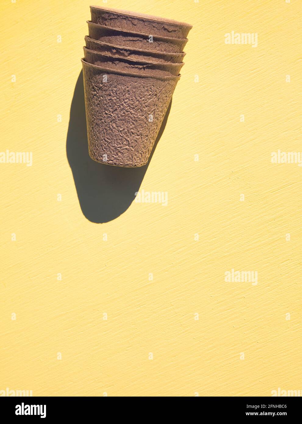 Stapel von biologisch abbaubaren Faser Torfpflanzen Töpfe im Sonnenlicht auf texturiertem gelben Hintergrund. Konzept von umweltfreundlich, nachhaltig, ohne Kunststoffe Stockfoto