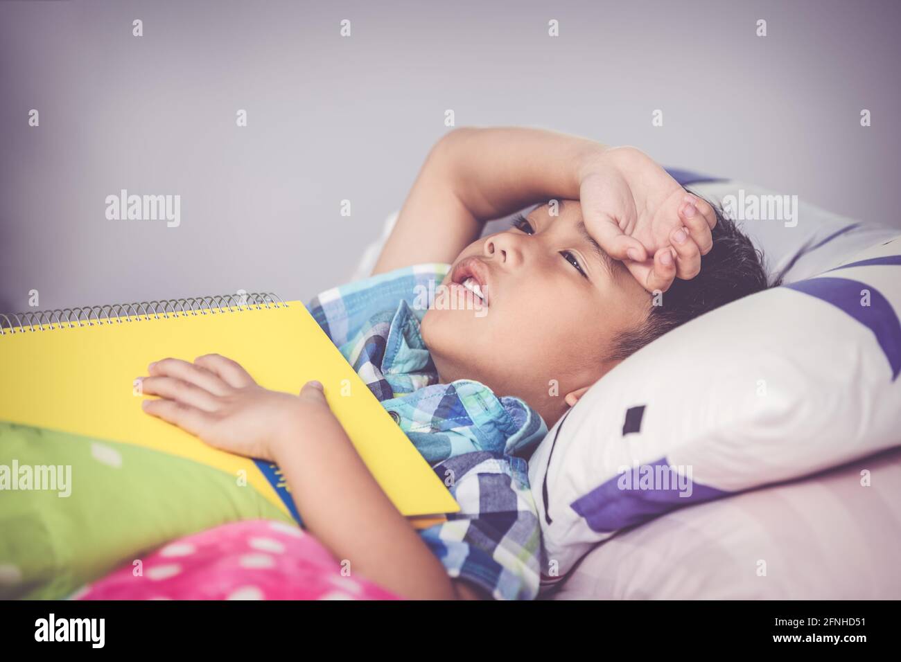 Müde und gelangweilt Kind unglücklich, als er ein Buch über das Bett im Schlafzimmer zu lesen. Kinder lesen und studieren, studieren hart, müde Schüler, Bildungskonzept. Vintage-T Stockfoto