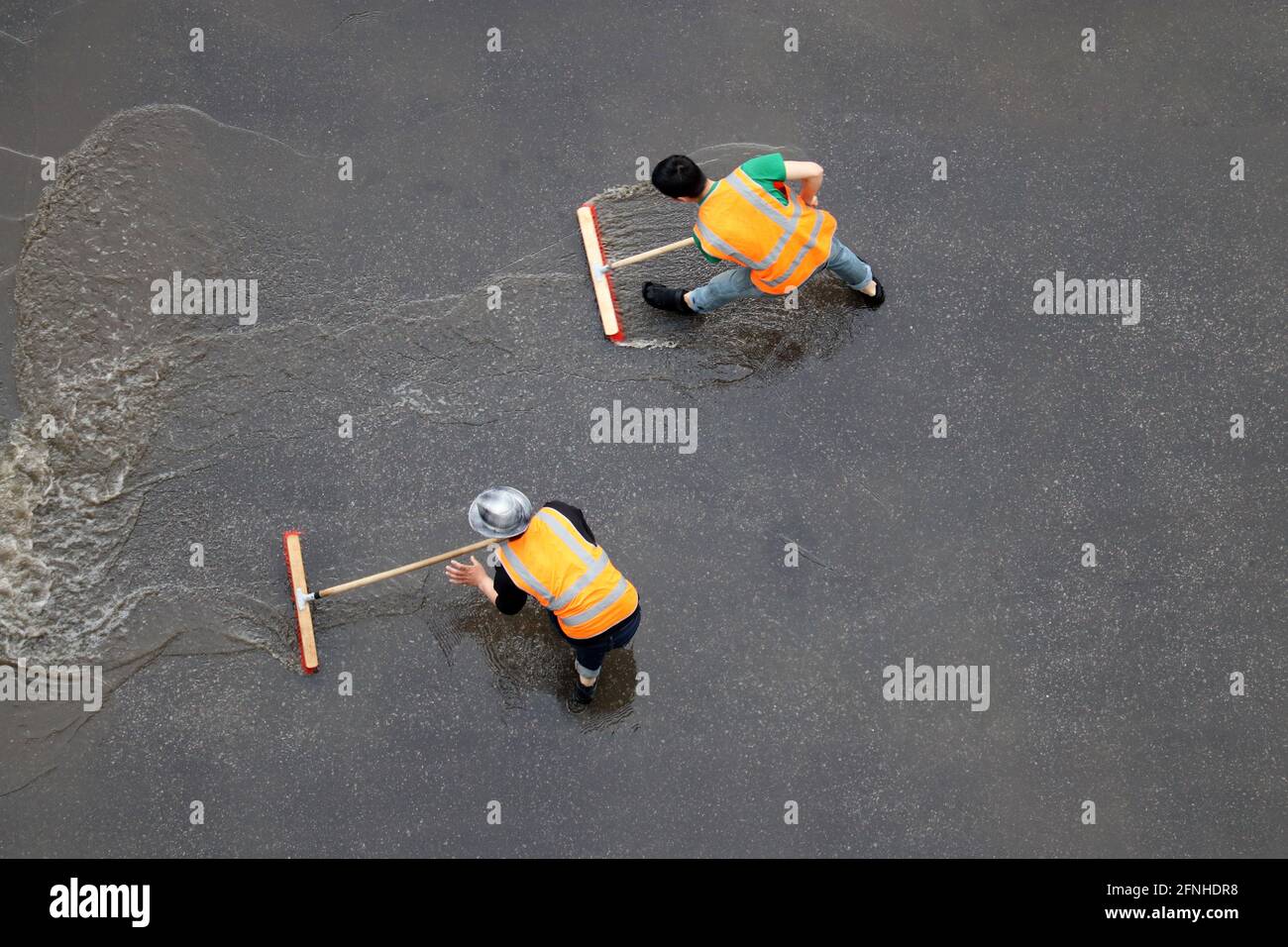 Zwei Arbeiter putzen nach dem Regen die Straße. Hausmeister mit Bürsten wäscht nasse Stadtstraße, Blick von oben Stockfoto