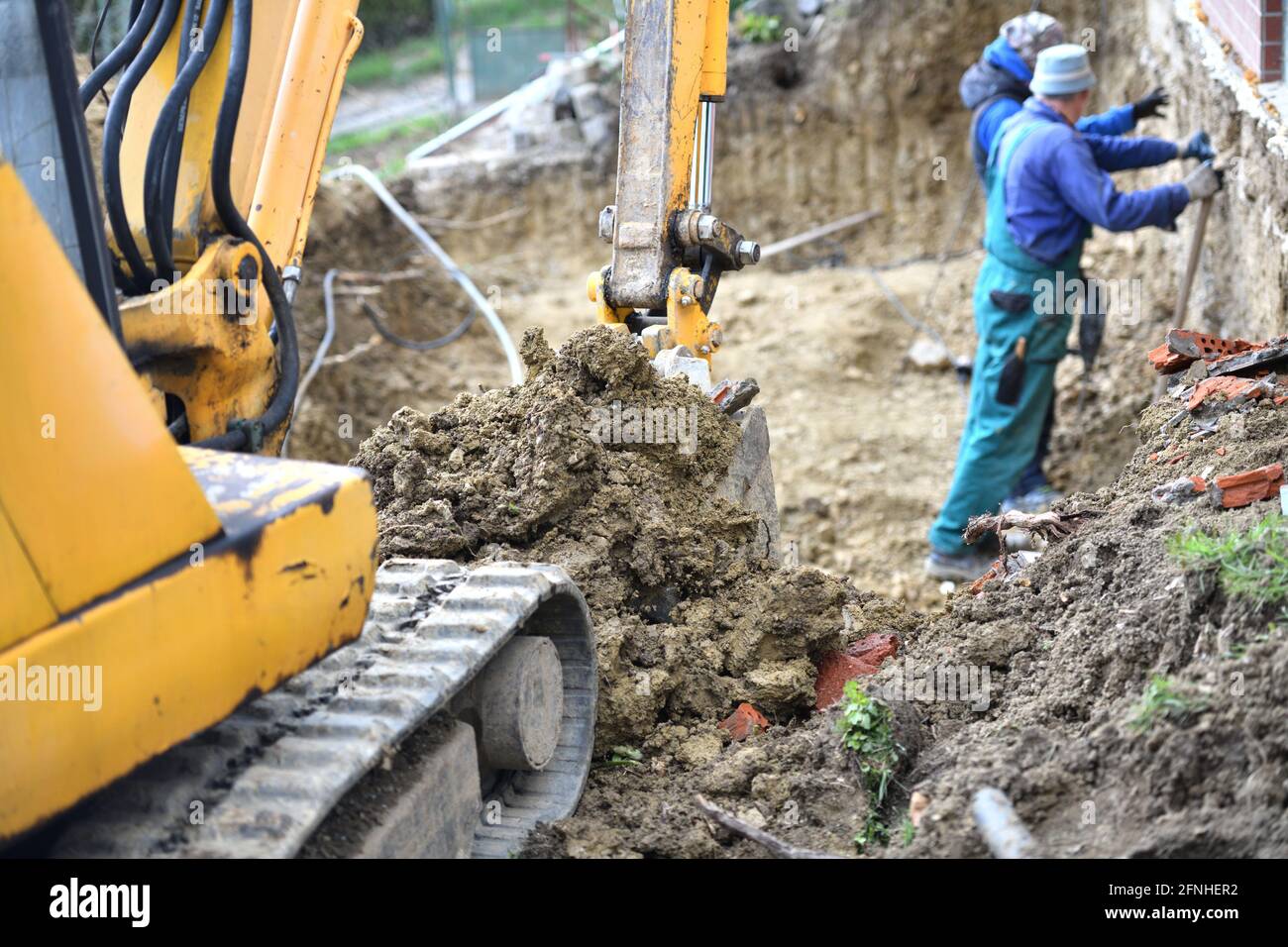 Ein Maurerarbeiter arbeitet auf einer Baustelle, während ein Baggerbagger im Hintergrund Stockfoto