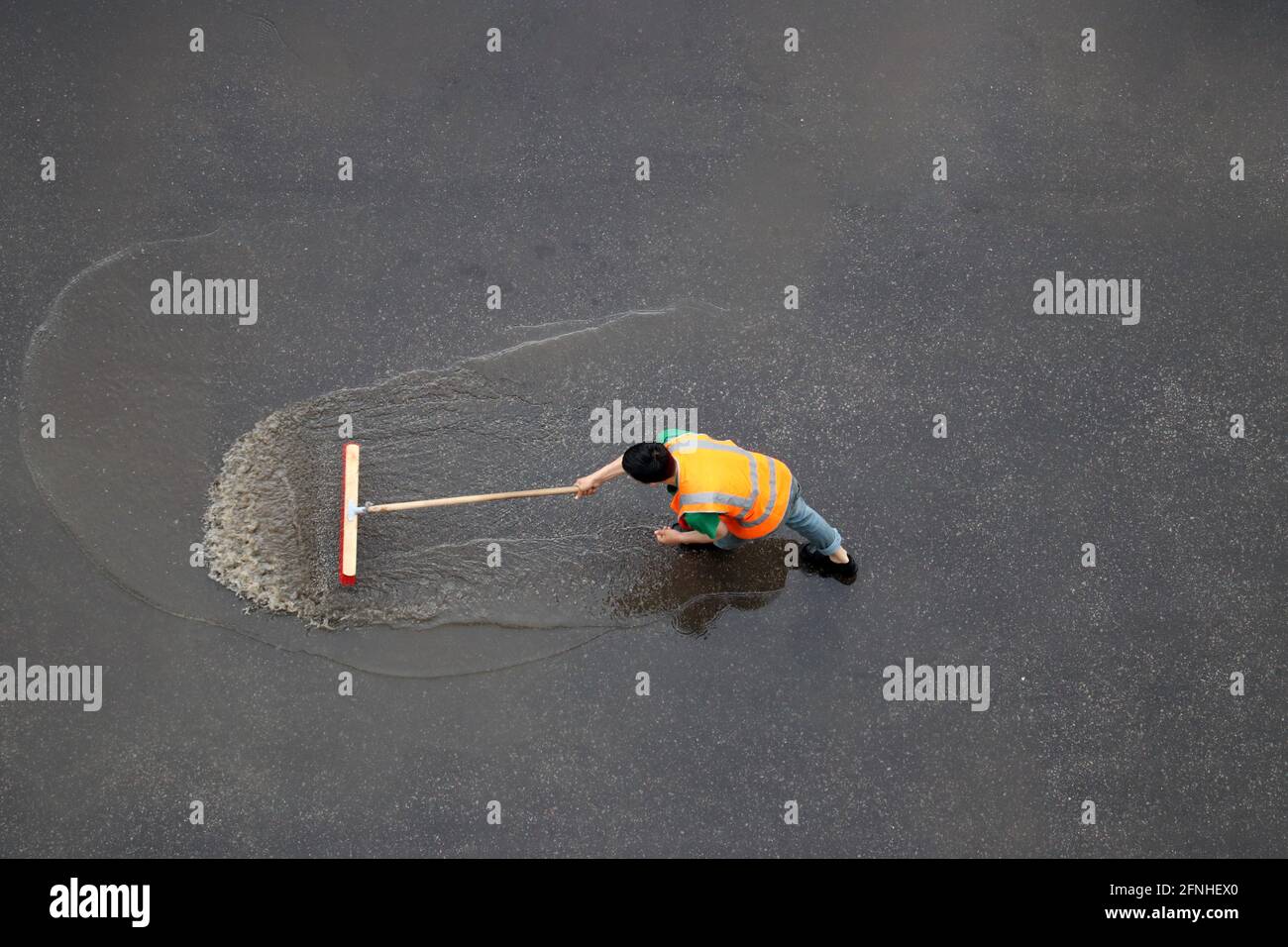 Arbeiter reinigt die Straße nach dem Regen. Hausmeister mit Pinsel wäscht nasse Stadtstraße, Blick von oben Stockfoto