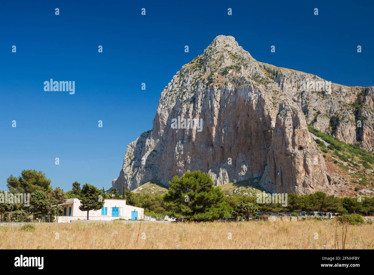 San Vito Lo Capo, Trapani, Sizilien, Italien. Isoliertes Dorfhaus, das von der aufragenden Nordwand des Monte Monaco in den Schatten gestellt wird. Stockfoto