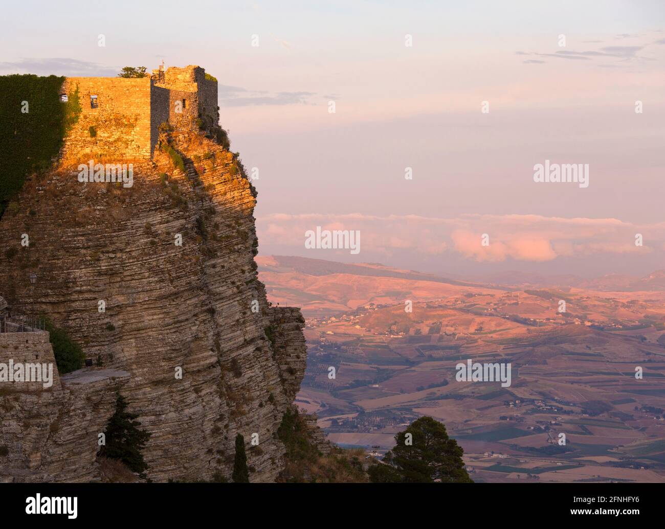 Erice, Trapani, Sizilien, Italien. Die Klippe Castello di Venere von der untergehenden Sonne beleuchtet, warmes Abendlicht auf landwirtschaftlichen Flächen dahinter. Stockfoto
