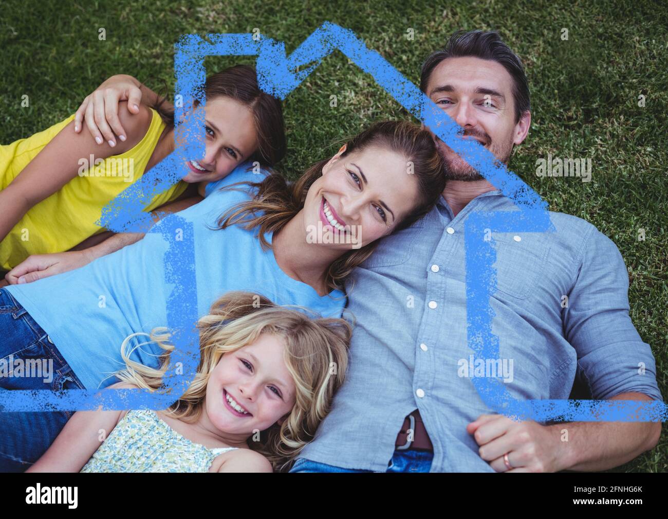 Glückliche kaukasische Familie, die sich im Gras mit Heimsymbol entspannt Stockfoto