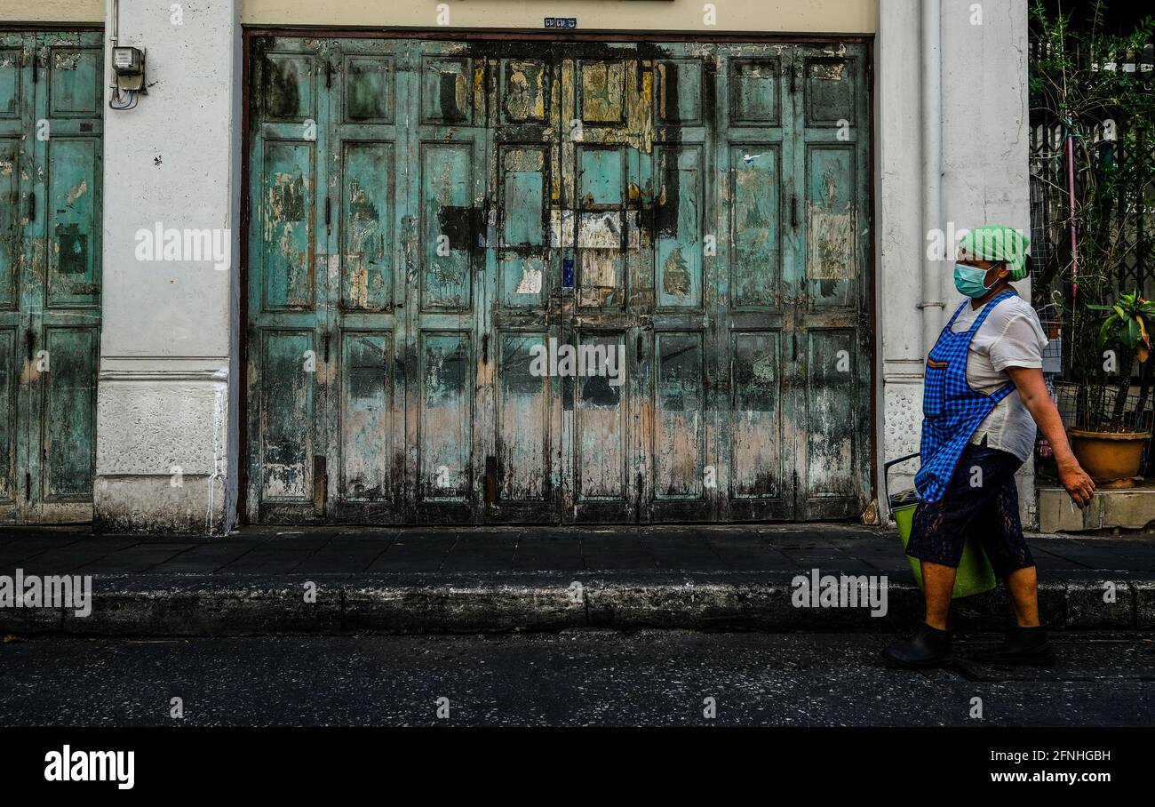 Eine ältere Arbeiterin, die einen Gesichtsbereich trägt, geht an einer alten, grün verwitterten Tür in der Chinatown-Gegend von Bangkok, Thailand, vorbei Stockfoto
