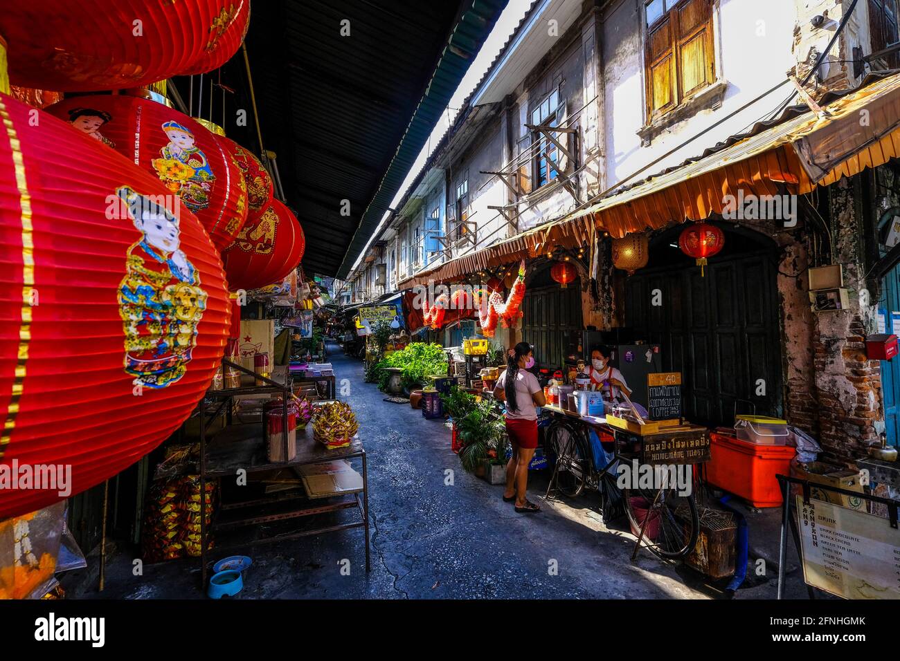 Die Menschen gehen in einer kleinen sonnenbeschienenen Gasse in Chinatown, Bangkok, Thailand, ihren täglichen Geschäften nach Stockfoto