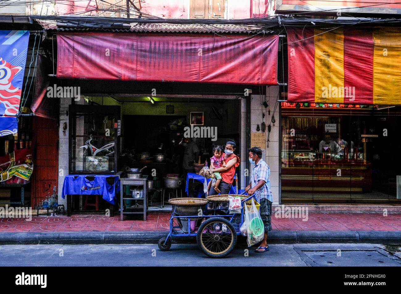 Ein männlicher Lebensmittelhändler verkauft Lebensmittel an eine Mutter und ein Kind in einer Straße in Chinatown, Bangkok, Thailand Stockfoto