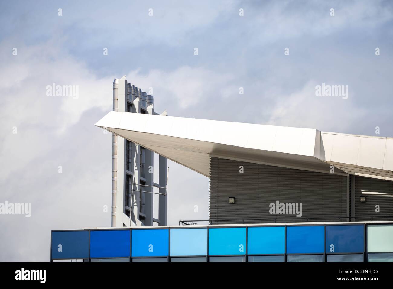 Moderne städtische Architektur in Blau- und Aqua-Bauweise, angewinkelte Dachlinie mit verchromten Edelstahlschornsteinen, die bis in den wolkenblauen Himmel reichen. Stockfoto